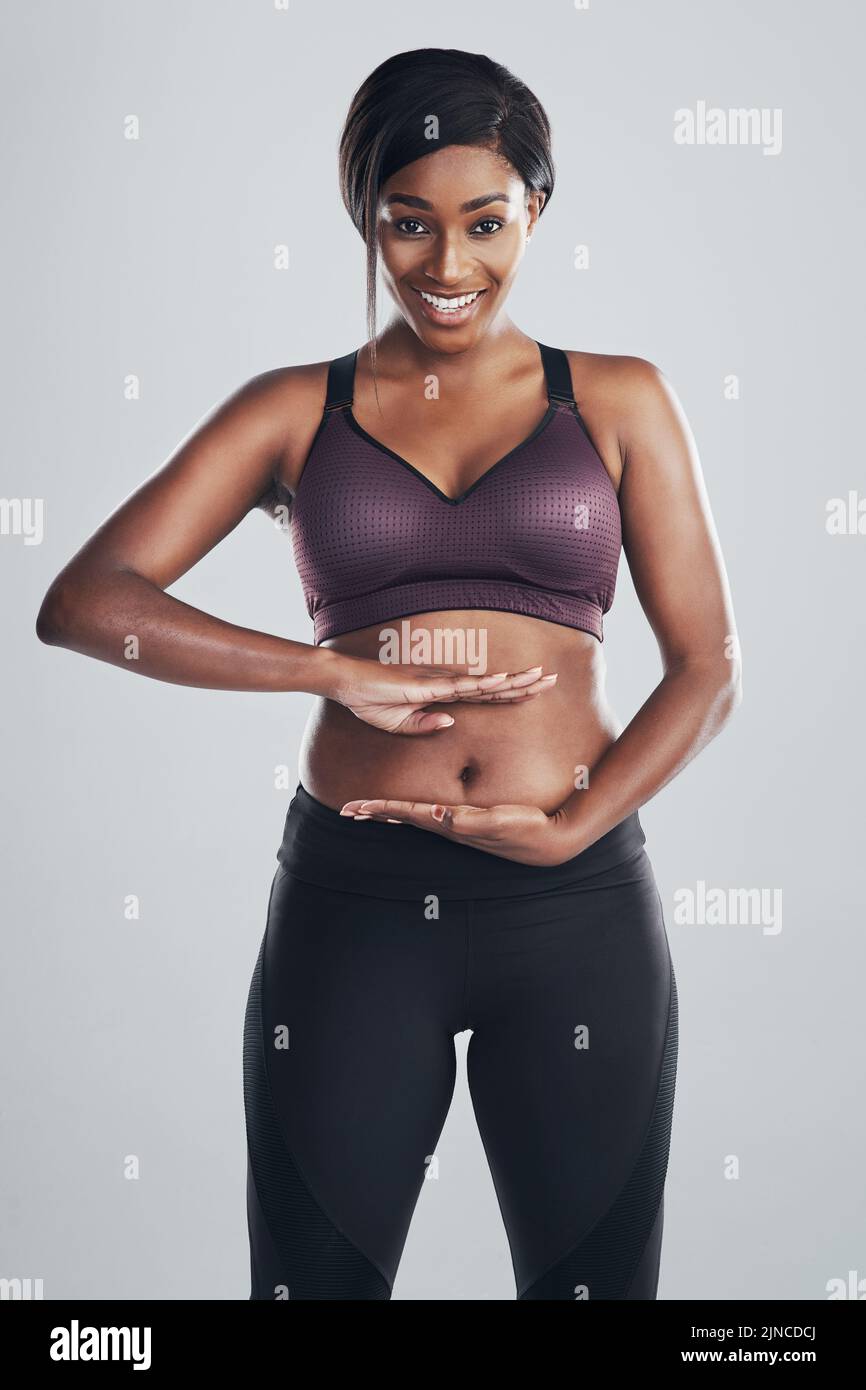 La beauté vient dans toutes les formes et tailles. Portrait studio d'une jeune femme attrayante et ajustée, encadrant son estomac avec ses mains contre un gris Banque D'Images
