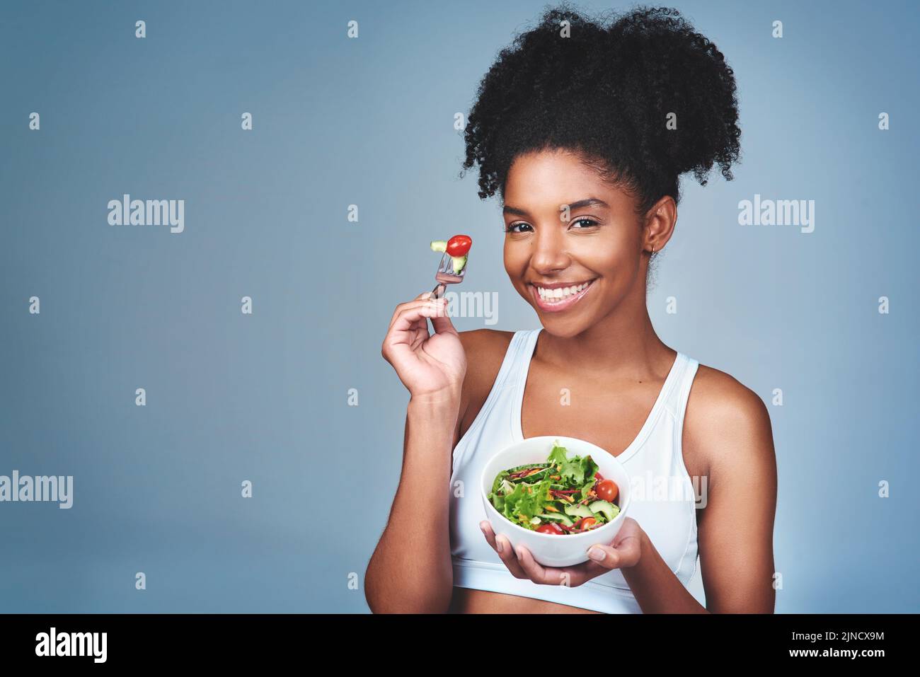 Vous voulez de la bonté. Photo en studio d'une jeune femme attrayante qui mange de la salade sur fond gris. Banque D'Images