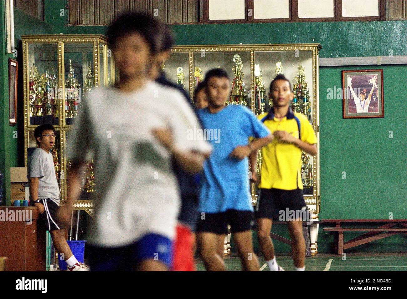De jeunes joueurs de badminton se réchauffent lors d'une séance d'entraînement au club de badminton Jaya Raya à Jakarta, en Indonésie, photographiés dans un fond d'armoire à trophées et une photo de l'ancien joueur vedette du club, Susi Susanti, médaillé d'or olympique. Banque D'Images