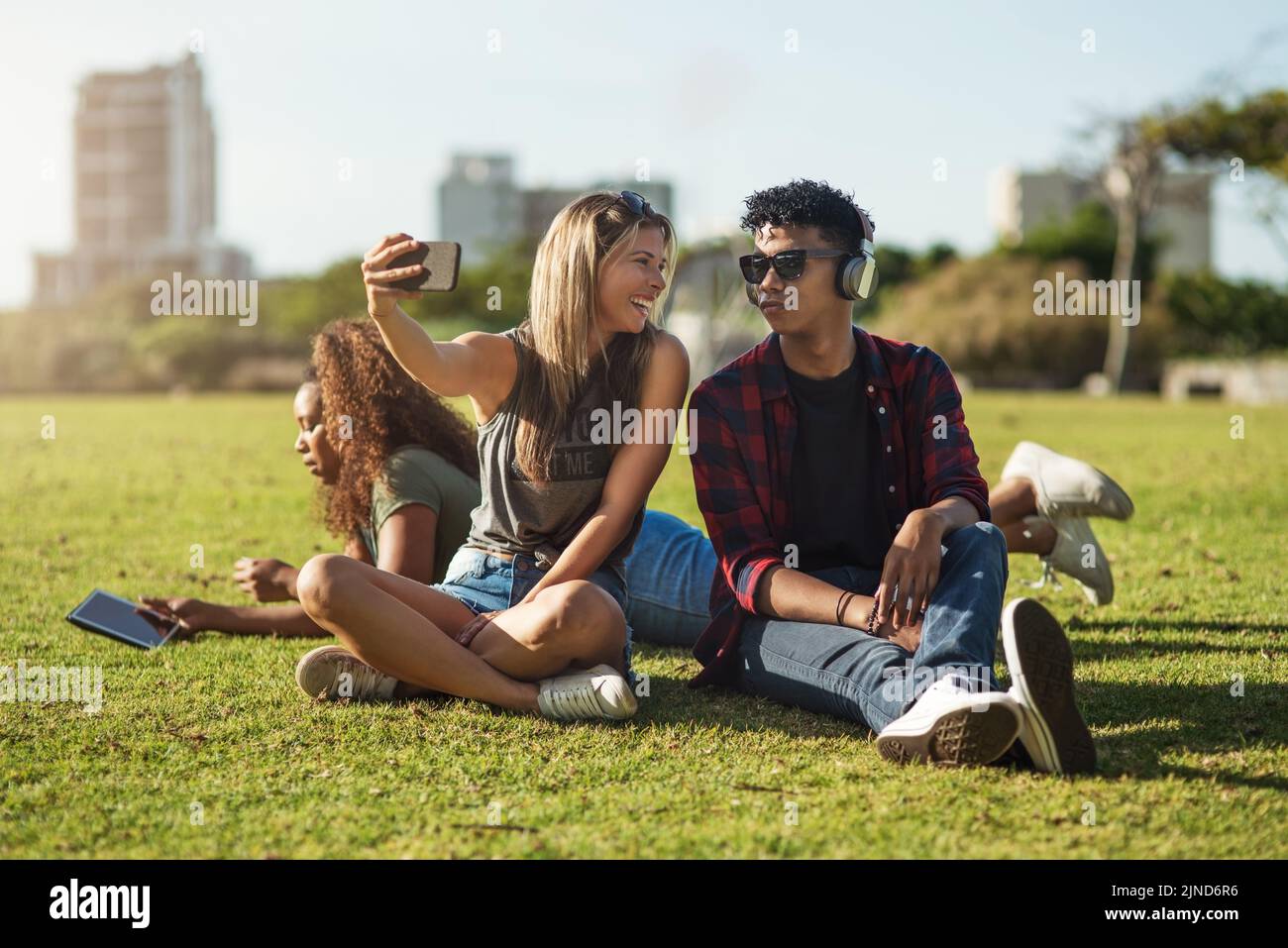 Regardez ici avec stupides. Deux jeunes amis joyeux prenant un autoportrait ensemble tout en écoutant de la musique sur des écouteurs à l'extérieur dans un parc. Banque D'Images