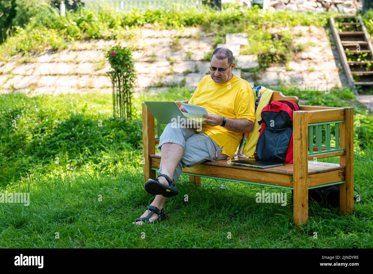 Homme mature avec ordinateur portable et documents travaillant à l'extérieur dans le jardin, concept de bureau à domicile vert. Banque D'Images