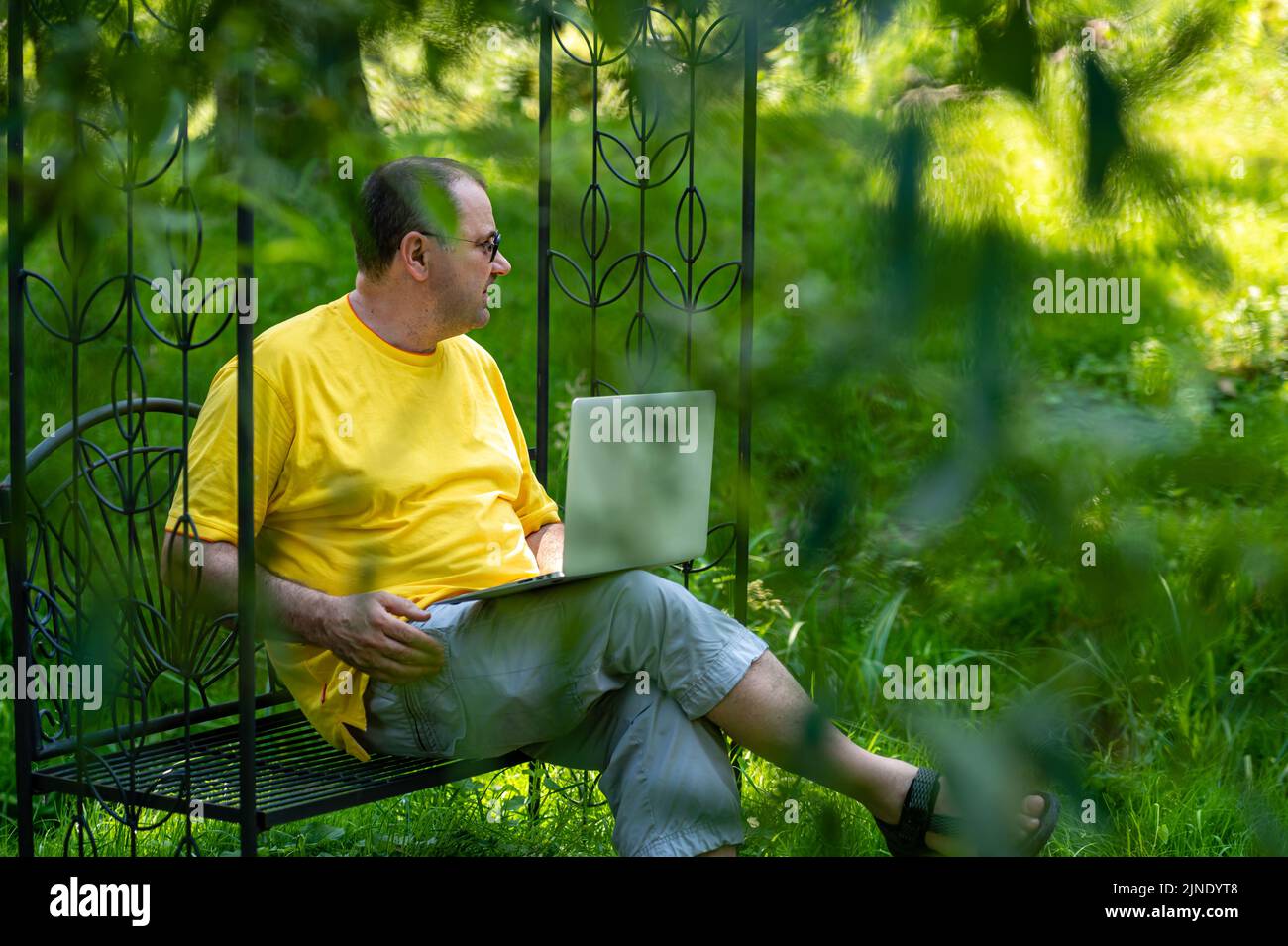 homme d'âge moyen avec ordinateur portable travaillant à l'extérieur dans le jardin, concept de bureau à domicile vert Banque D'Images
