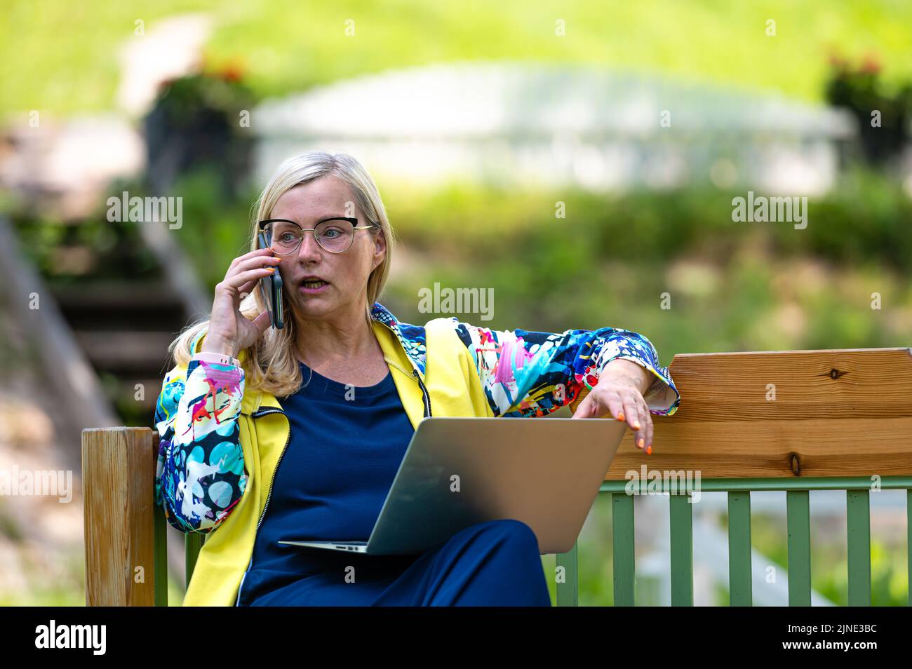 femme âgée dans le jardin travaillant à la maison en utilisant un ordinateur portable et parlant au téléphone Banque D'Images