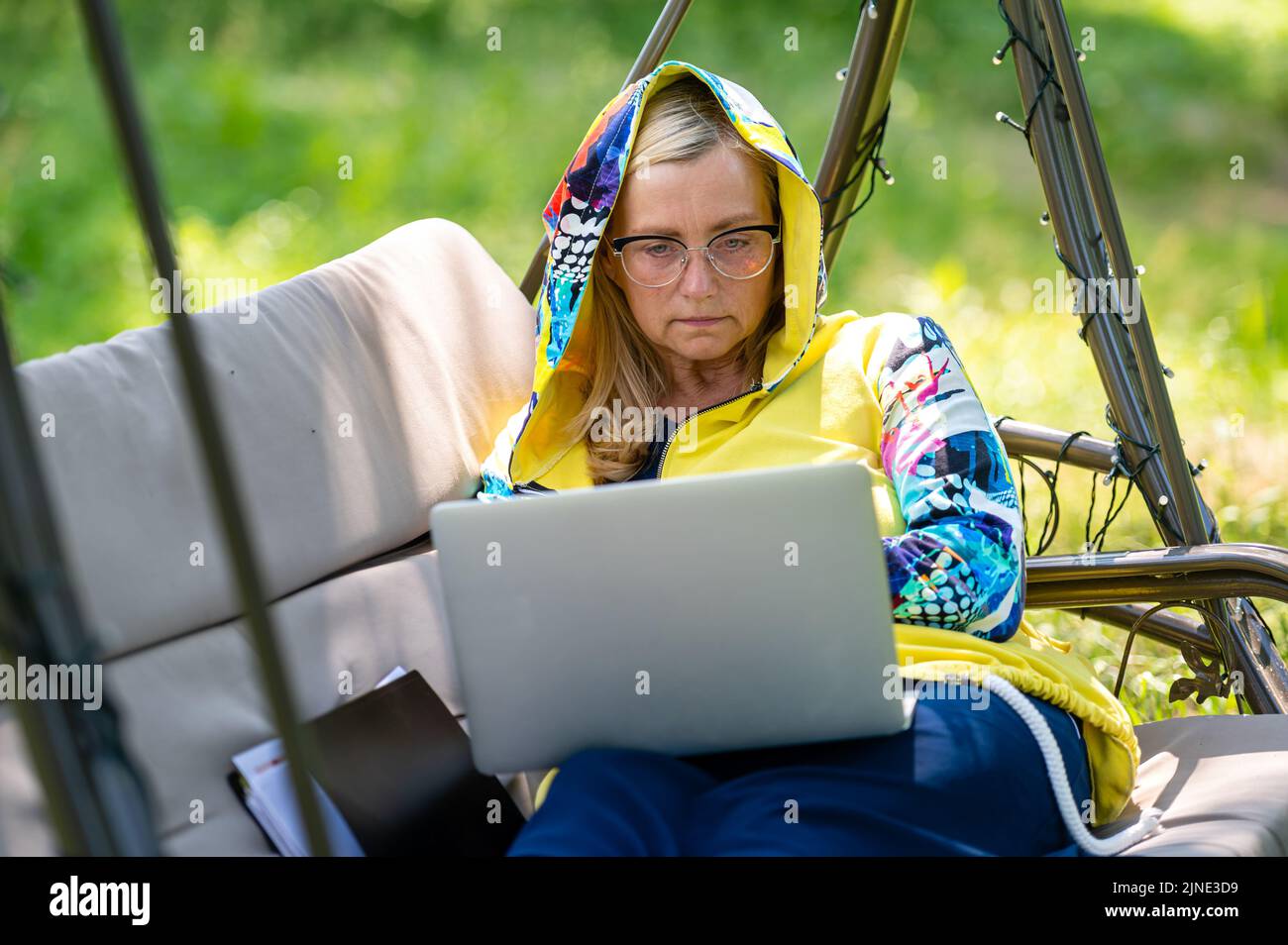 femme mature avec ordinateur portable et documents travaillant dans le jardin sur un canapé à bascule, concept vert de bureau à domicile Banque D'Images