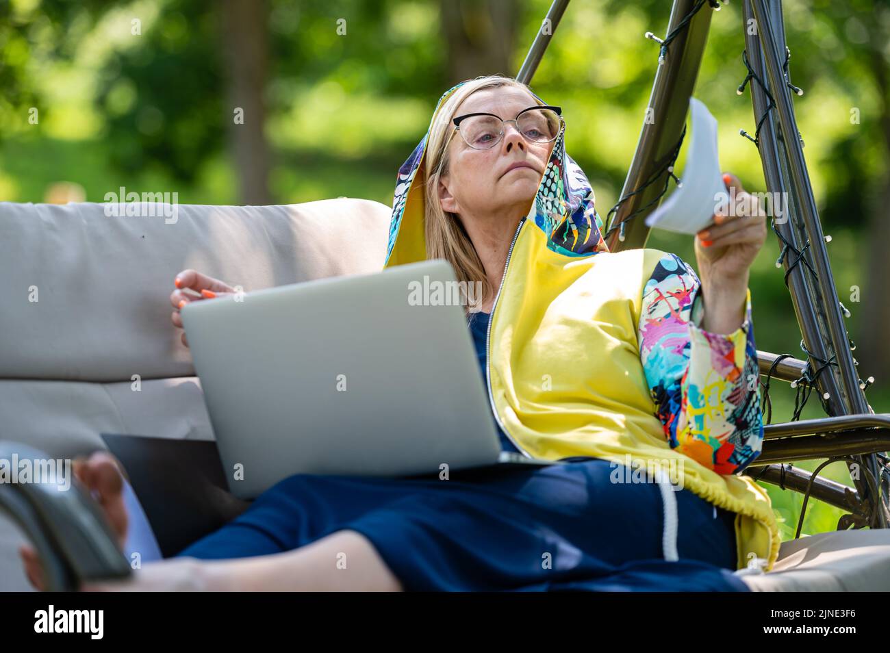 femme mature avec ordinateur portable et documents travaillant dans le jardin sur un canapé à bascule, concept vert de bureau à domicile Banque D'Images