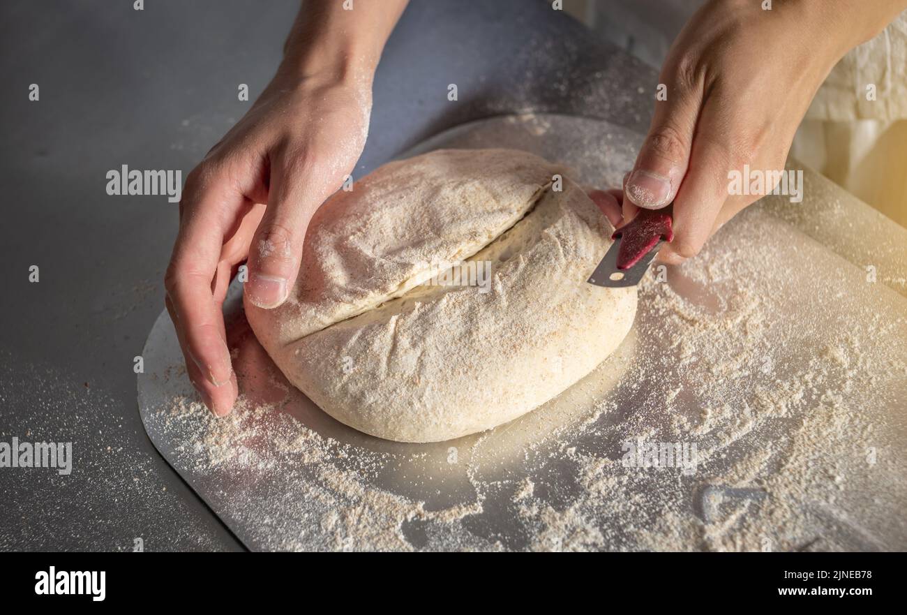 Un boulanger mâle coupe la pâte à l'aide d'un couteau avant d'entrer dans le four pour la cuisson. Production de produits de boulangerie en tant que petite entreprise. Banque D'Images