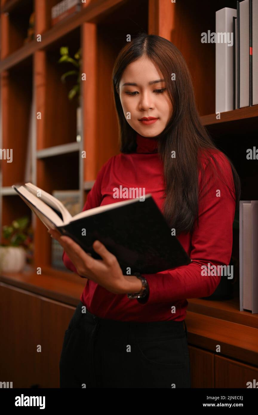Portrait, belle et magnifique femme asiatique lisant un livre tout en trouvant un livre sur l'étagère dans la bibliothèque. Banque D'Images
