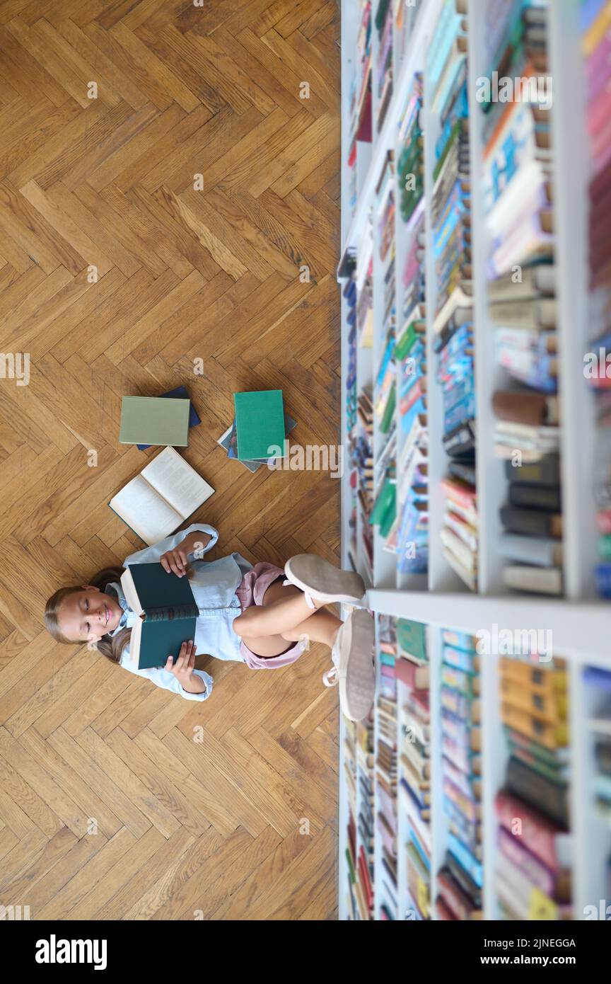 Une adolescente souriante perce un livre dans la bibliothèque Banque D'Images