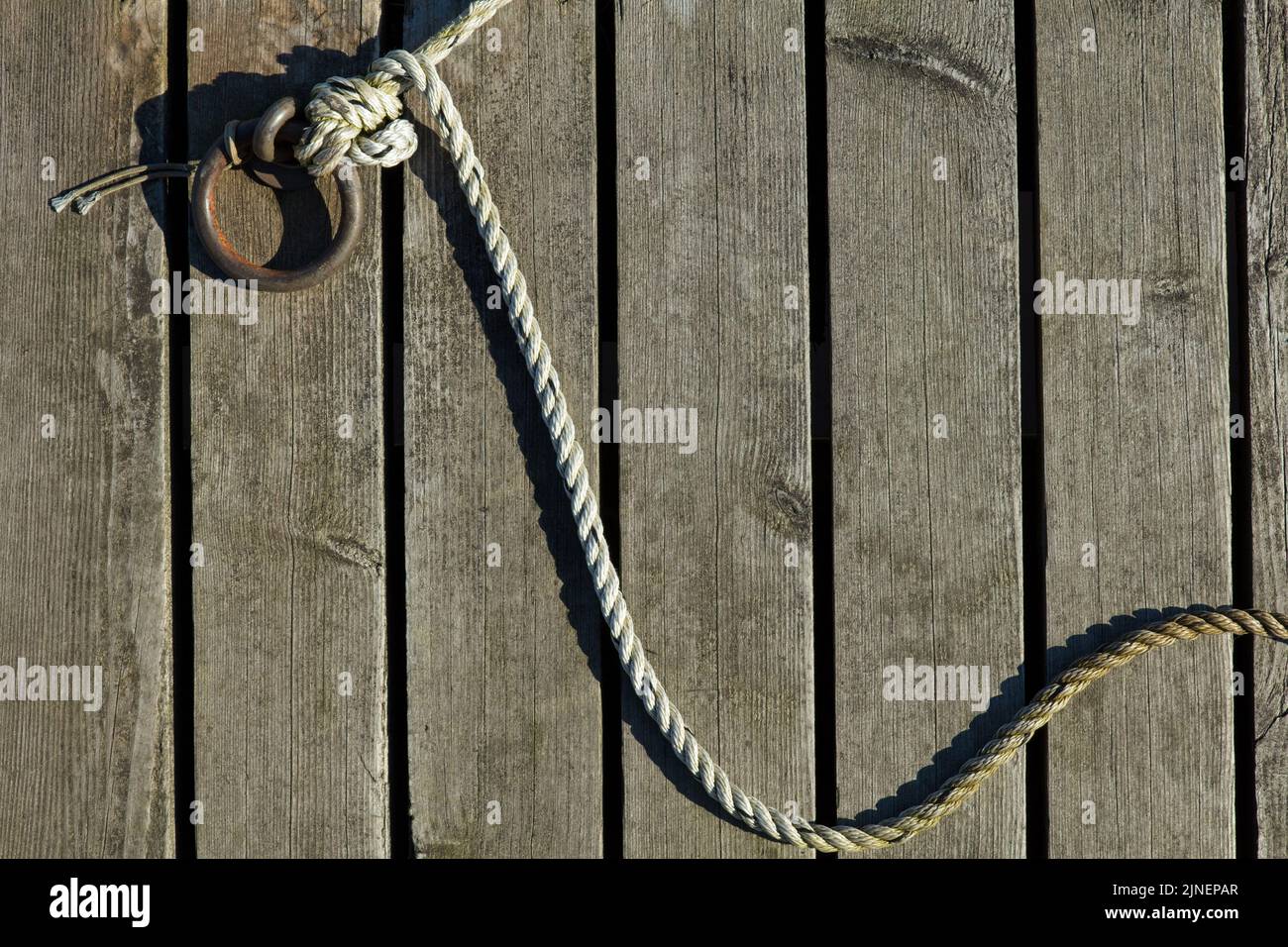 Corde fixée à un anneau d'amarrage en métal sur une jetée en bois. Banque D'Images