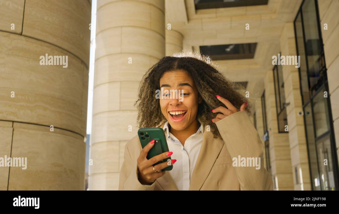 Bonne femme d'affaires afro-américaine dans une veste regarde un smartphone, lire les bonnes nouvelles ou obtenir une promotion Banque D'Images