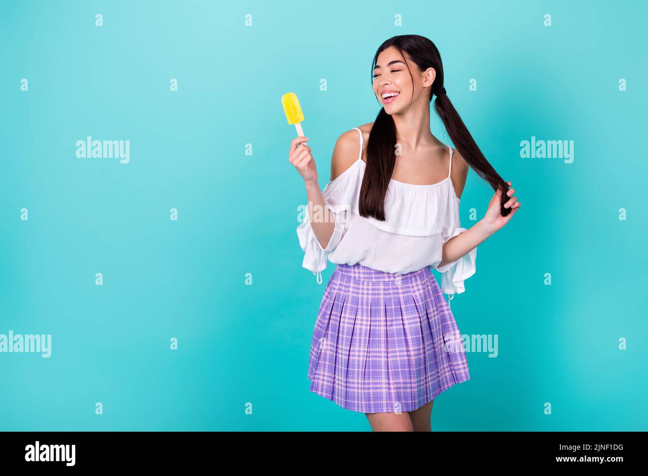 Photo d'une adorable dame de l'école en appréciant un rafraîchissement d'été tenir le popsicle isolé couleur cyan fond Banque D'Images