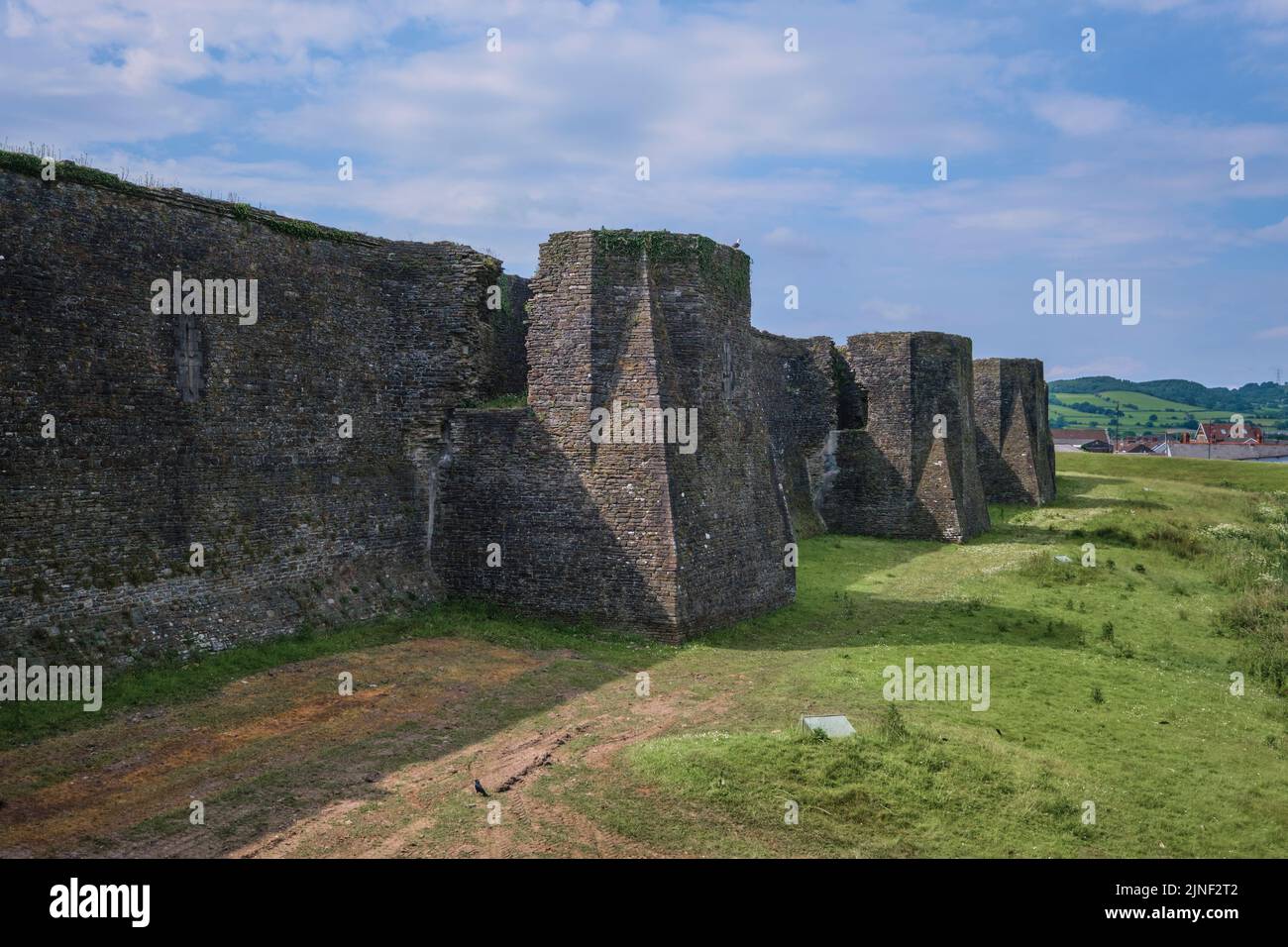 Vue sur les fortifications et tourelles du mur extérieur en pierre avec le fossé sec, maintenant la pelouse, l'herbe. Au château de Caerphilly à Caerphilly, Royaume-Uni. Banque D'Images