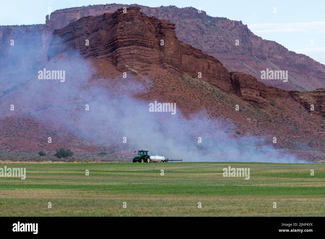 Un tracteur tirant un brûleur de propane brûle les mauvaises herbes dans un champ de foin après avoir coupé la luzerne dans un ranch de l'Utah. Banque D'Images