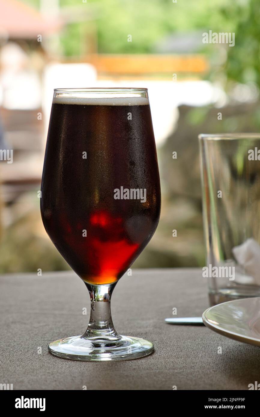 Verre de bière d'ambre foncé sur la table dans le restaurant extérieur d'été. Orange artisanal. Banque D'Images