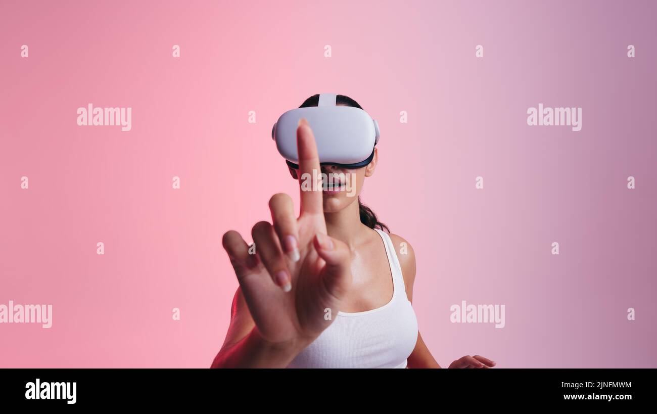 Toucher le métaverse. Jeune femme utilisant son doigt pour toucher l'espace virtuel tout en portant un casque de réalité virtuelle. Femme explorant la technologie 3D dans Banque D'Images