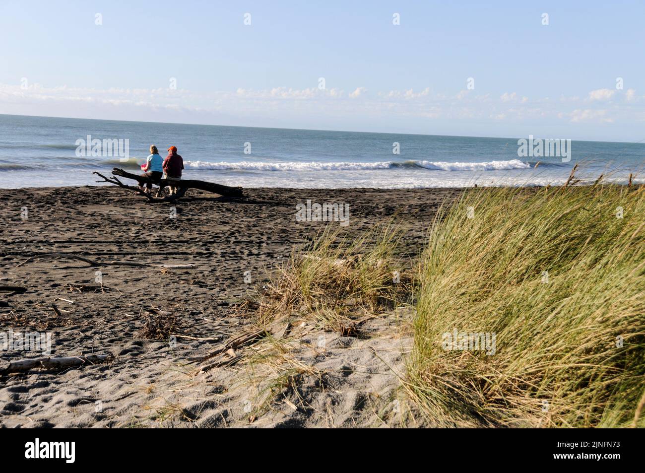 Un couple en vacances, assis sur un morceau de bois de grève sur la plage de Hokitika, regardant le soleil se coucher sur la mer de Tasman à Hokitika, sur la côte ouest de Banque D'Images