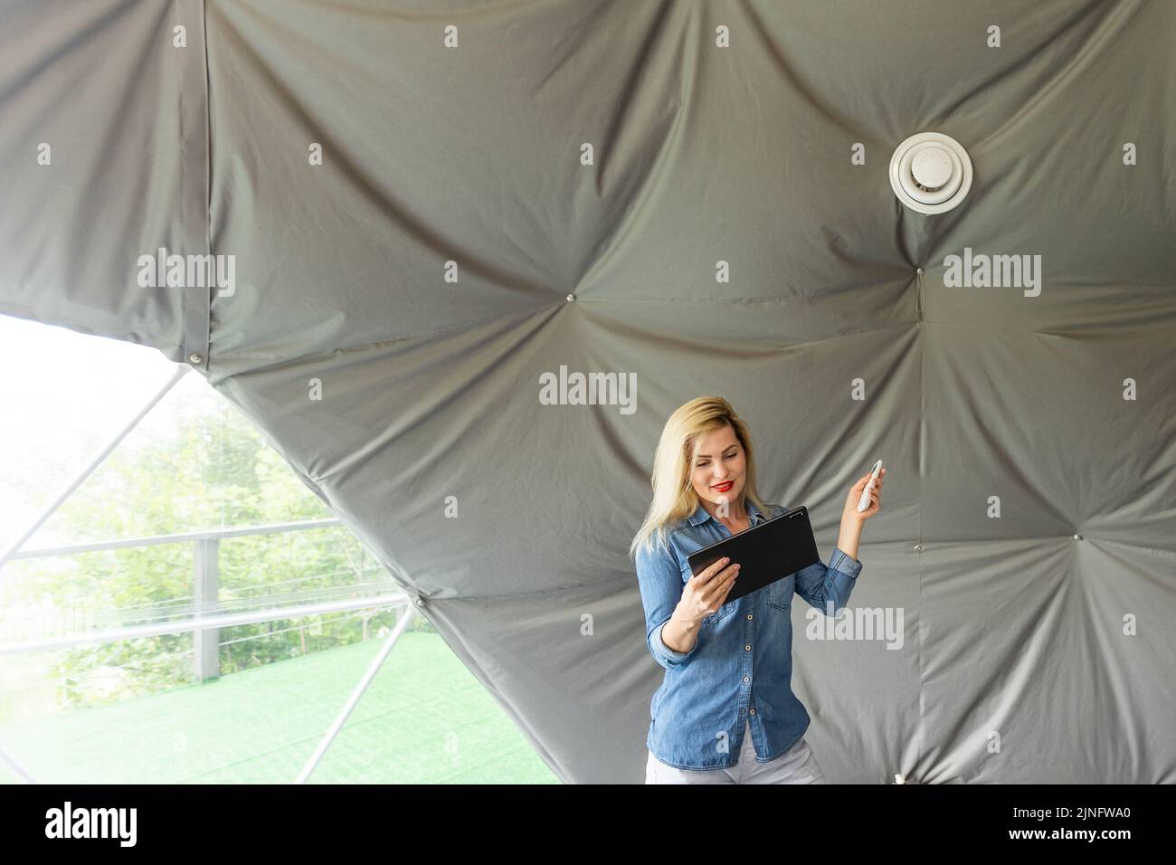 femme avec une tablette qui active le système de ventilation comme récupérateur pour la qualité de l'air frais à l'intérieur, maison intelligente Banque D'Images