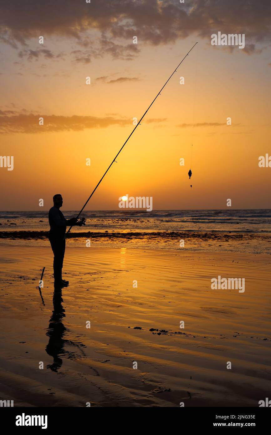 Un Fisher tenant son crochet avec sa tige de pêcheur avec un beau coucher de soleil dans la ville de Laayoune Banque D'Images Un Fisher tenant son crochet avec sa tige de pêcheur avec un beau coucher de soleil dans la ville de Laayoune Banque D'Images