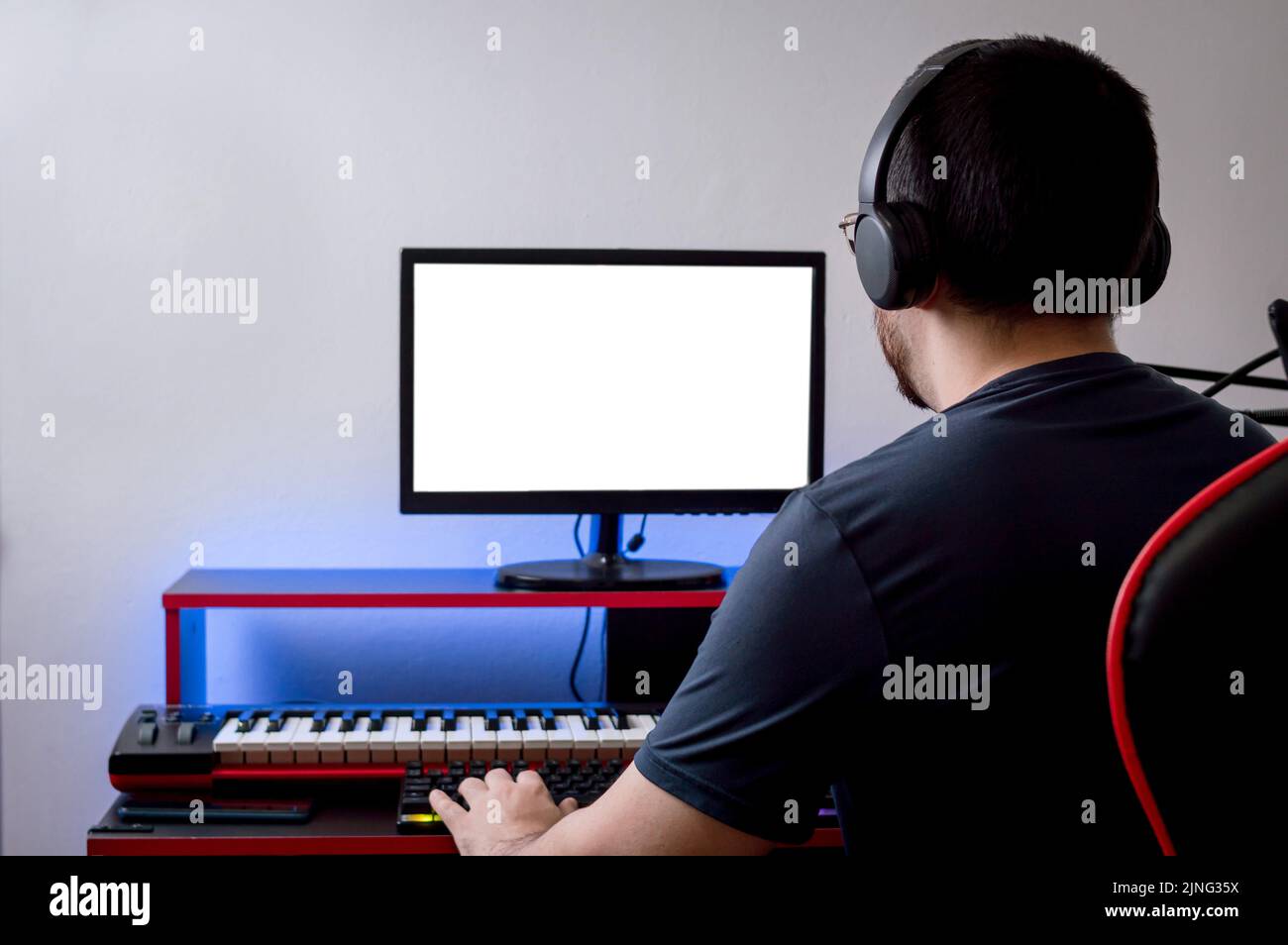 vue arrière du jeune homme caucasien avec casque regardant l'écran d'ordinateur avec une main sur le clavier, dans son studio de musique à la maison, la technologie et Banque D'Images