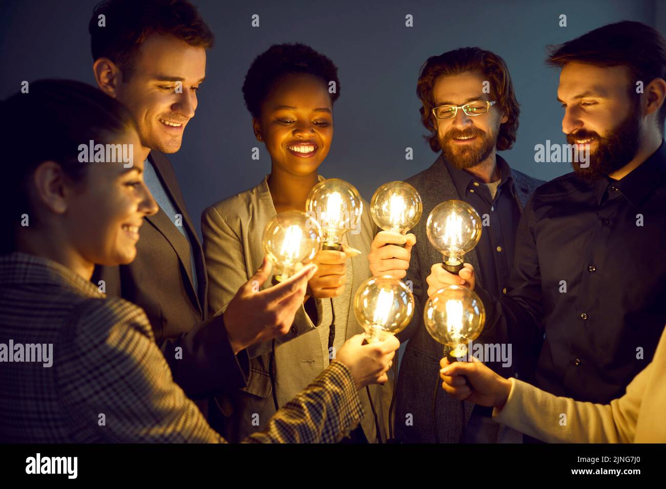 Un groupe de personnes intelligentes et heureuses tient des ampoules brillantes comme symbole d'idées créatives. Banque D'Images