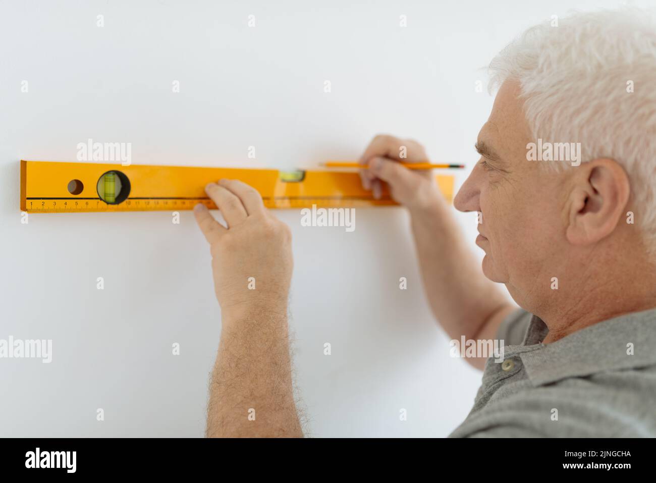 Homme senior mesurant mur avec niveau de construction Banque D'Images