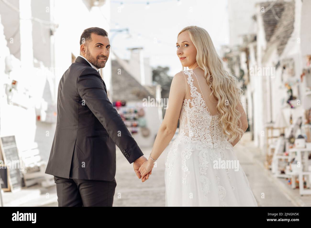 Portrait de couple marchant, regardant en arrière. Bonne mariée portant une longue robe blanche aux mains assorties avec le marié en costume. Banque D'Images Portrait de couple marchant, regardant en arrière. Bonne mariée portant une longue robe blanche aux mains assorties avec le marié en costume. Banque D'Images