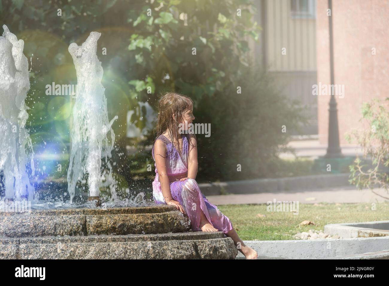 Petite fille adorable éclaboussant dans une fontaine d'été. Banque D'Images