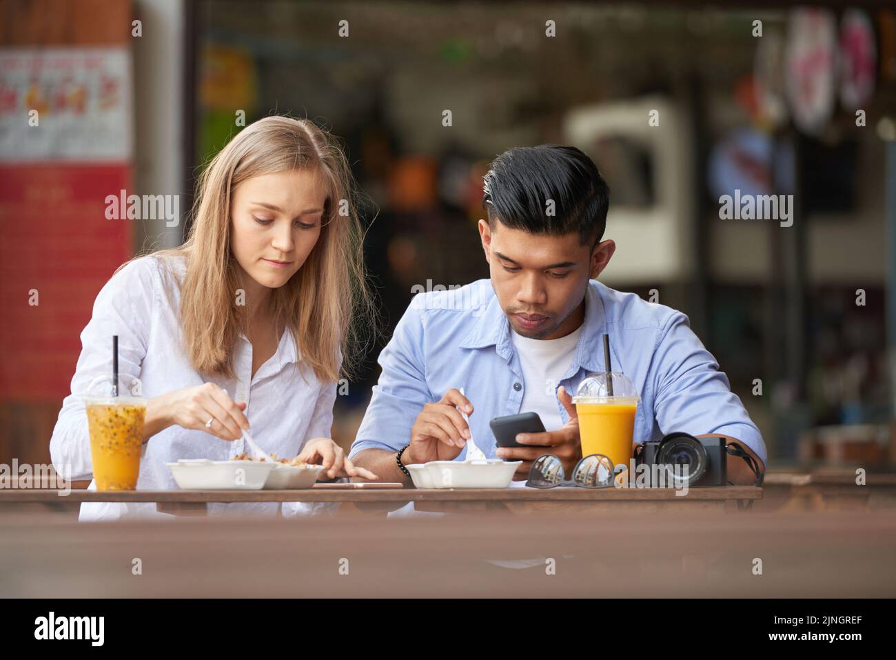 Jeune couple de touristes mangeant de la nourriture de rue asiatique, homme utilisant son smartphone Banque D'Images
