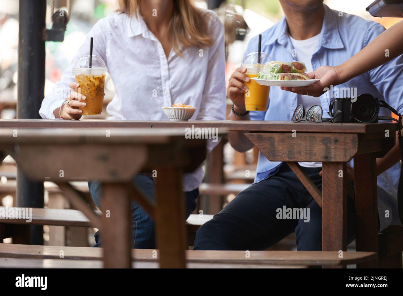 Une serveuse méconnue apporte de la nourriture pour un jeune couple au café en plein air Banque D'Images