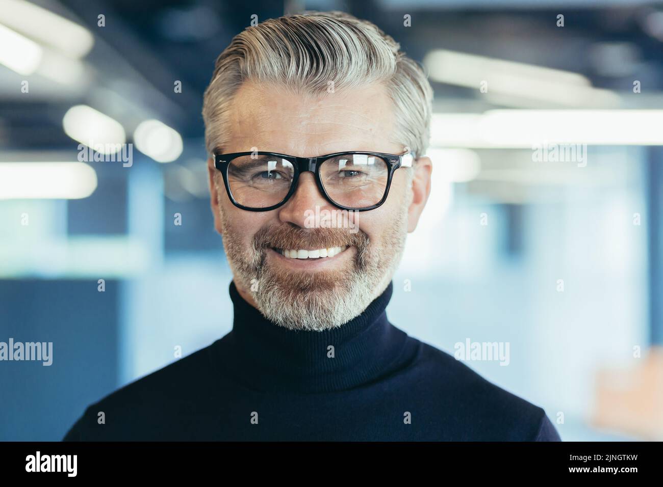 Portrait en gros plan d'un homme d'affaires à cheveux gris heureux et réussi, investisseur masculin avec des lunettes et une barbe regardant l'appareil photo et souriant, patron travaillant dans un bureau moderne Banque D'Images