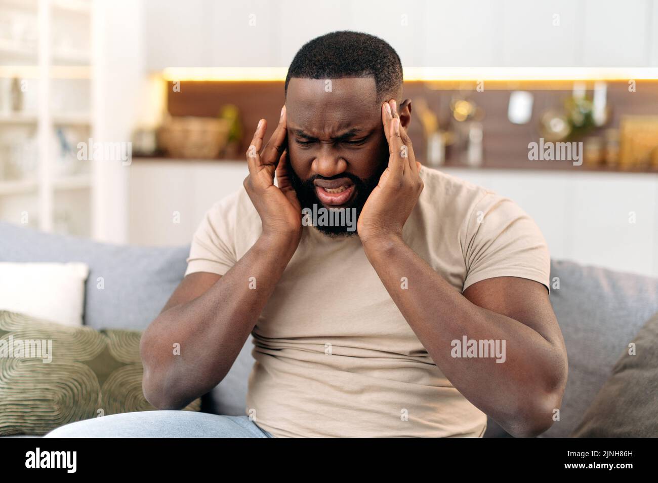 Maux de tête, crampes. Frustré épuisé africain américain homme, assis sur le canapé dans le salon, massages de ses temples, fermé ses yeux, se sent mal, migraine, fatigue, besoin de traitement et de repos Banque D'Images