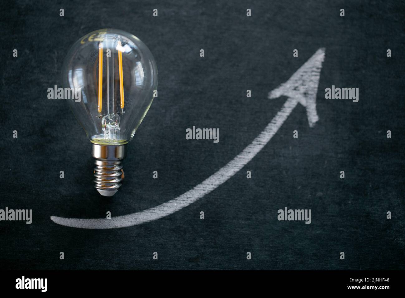Crise de la production d'énergie. Hausse des prix de l'électricité.ampoule et de l'arrowon sur un tableau noir de craie.coût de l'électricité.augmentation du coût de la lumière Banque D'Images