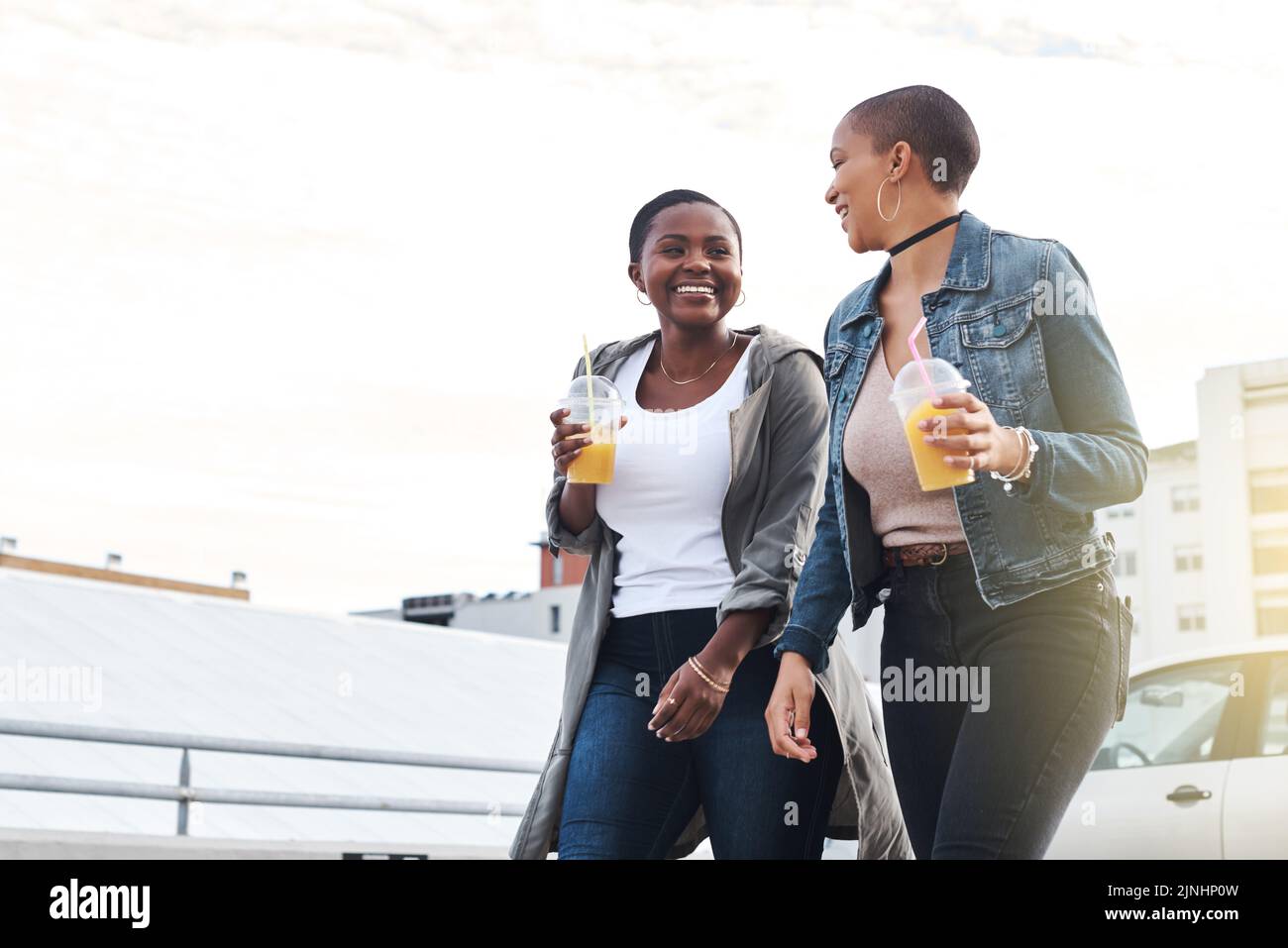 Côte à côte à chaque étape. Photo sous angle de deux jeunes femmes marchant dans la ville en riant tout en tenant leurs boissons fraîches. Banque D'Images