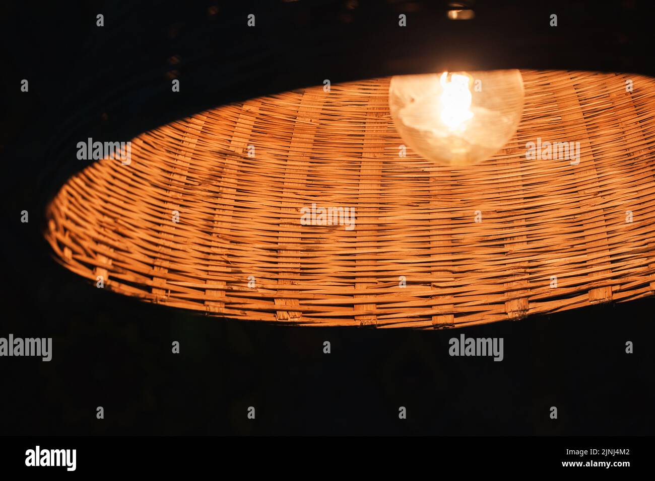 Lampe au tungstène vintage dans un abat-jour rond en osier illuminant dans la sombre, photo de gros plan avec mise au point sélective Banque D'Images