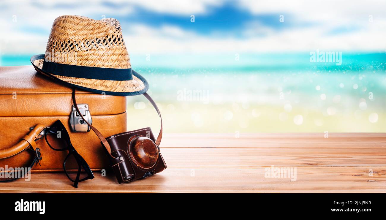 Valise vintage, lunettes de soleil et chapeau hipster terrasse en bois et fond de mer tropical flou. Bannière de mise en page de la croisière Summer Paradise. Tourisme, Banque D'Images