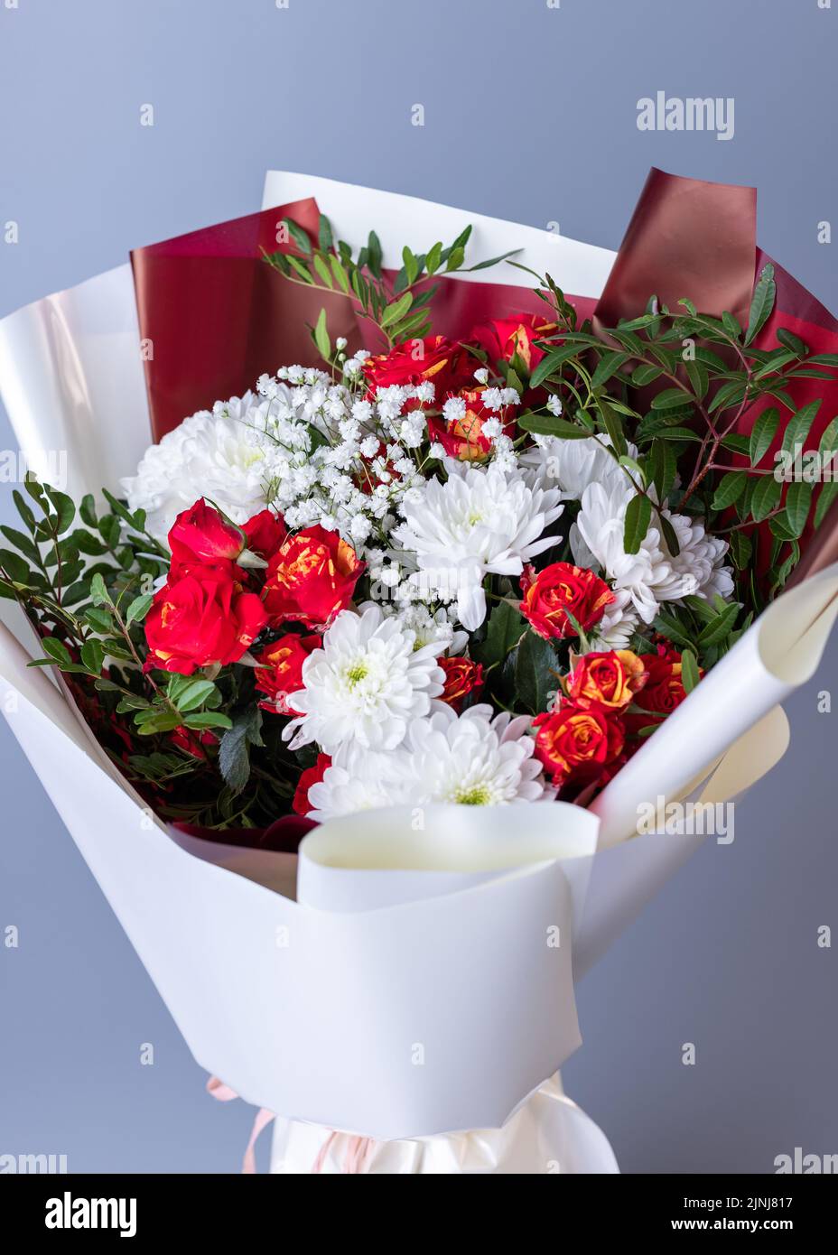 Arrangements floraux. Gros plan de fleurs blanches et rouges enveloppées de papier floral brillant sur fond bleu. Bouquet de roses roses, chrysanthèmes blancs, Banque D'Images