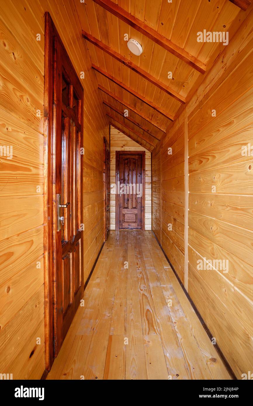 Couloir minimaliste lumineux avec un plafond en pente dans lequel les entrées avec des portes massives aux chambres dans un chalet en bois. Banque D'Images