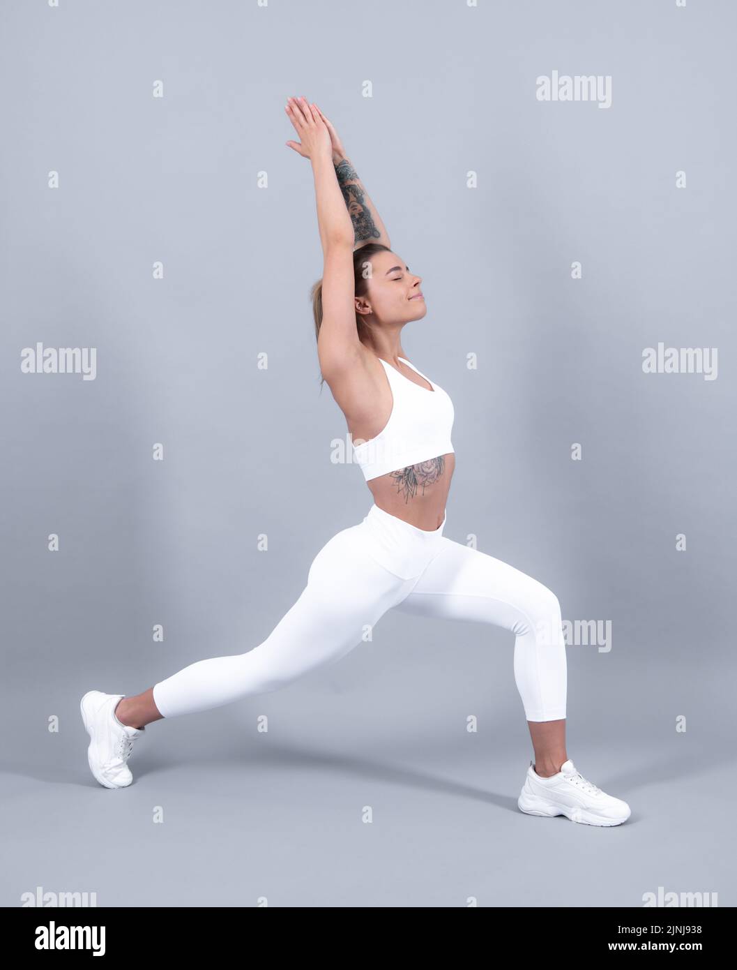 Femme en vêtements de sport qui s'étire. Fille s'étirant avant l'entraînement sur fond gris studio. Banque D'Images