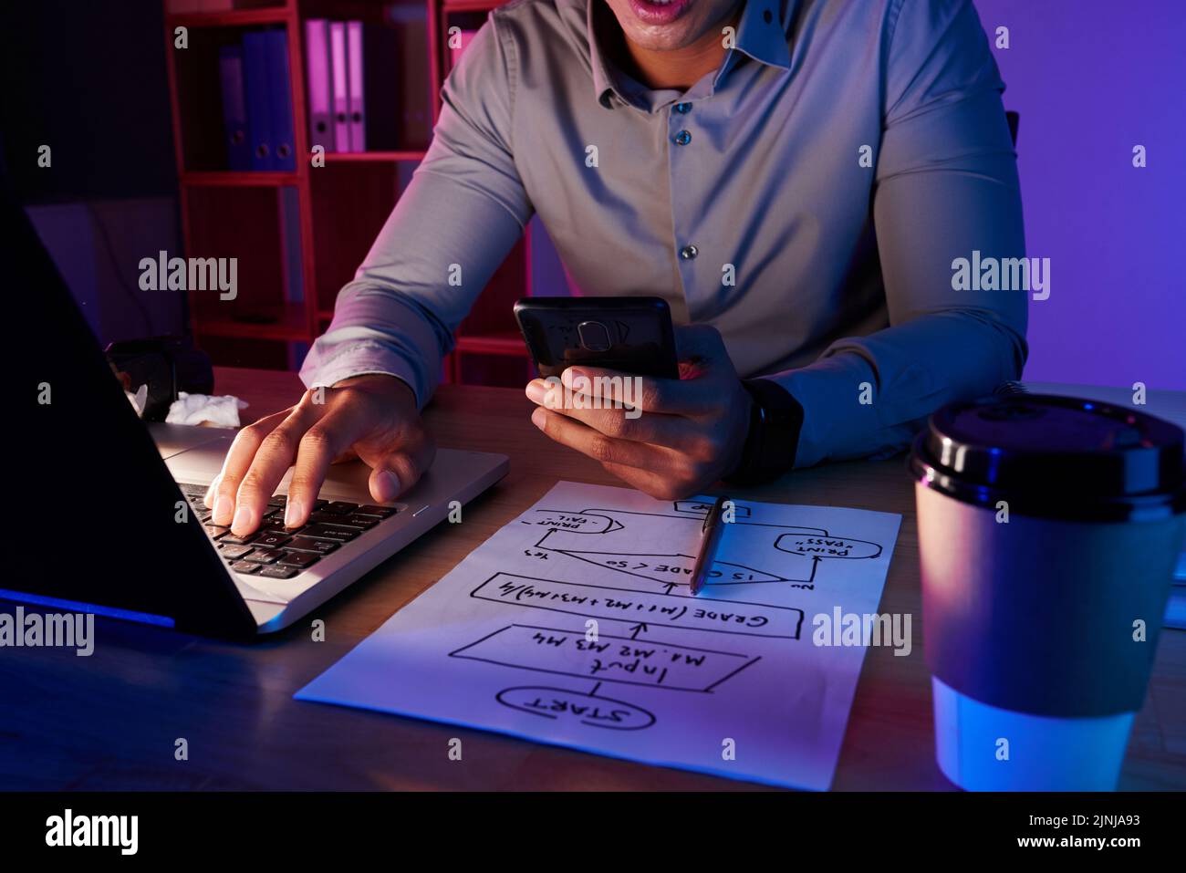 Travailleur de col blanc méconnaissable assis au bureau de dim et en composant le numéro du client tout en travaillant sur un projet ambitieux, gros plan Banque D'Images