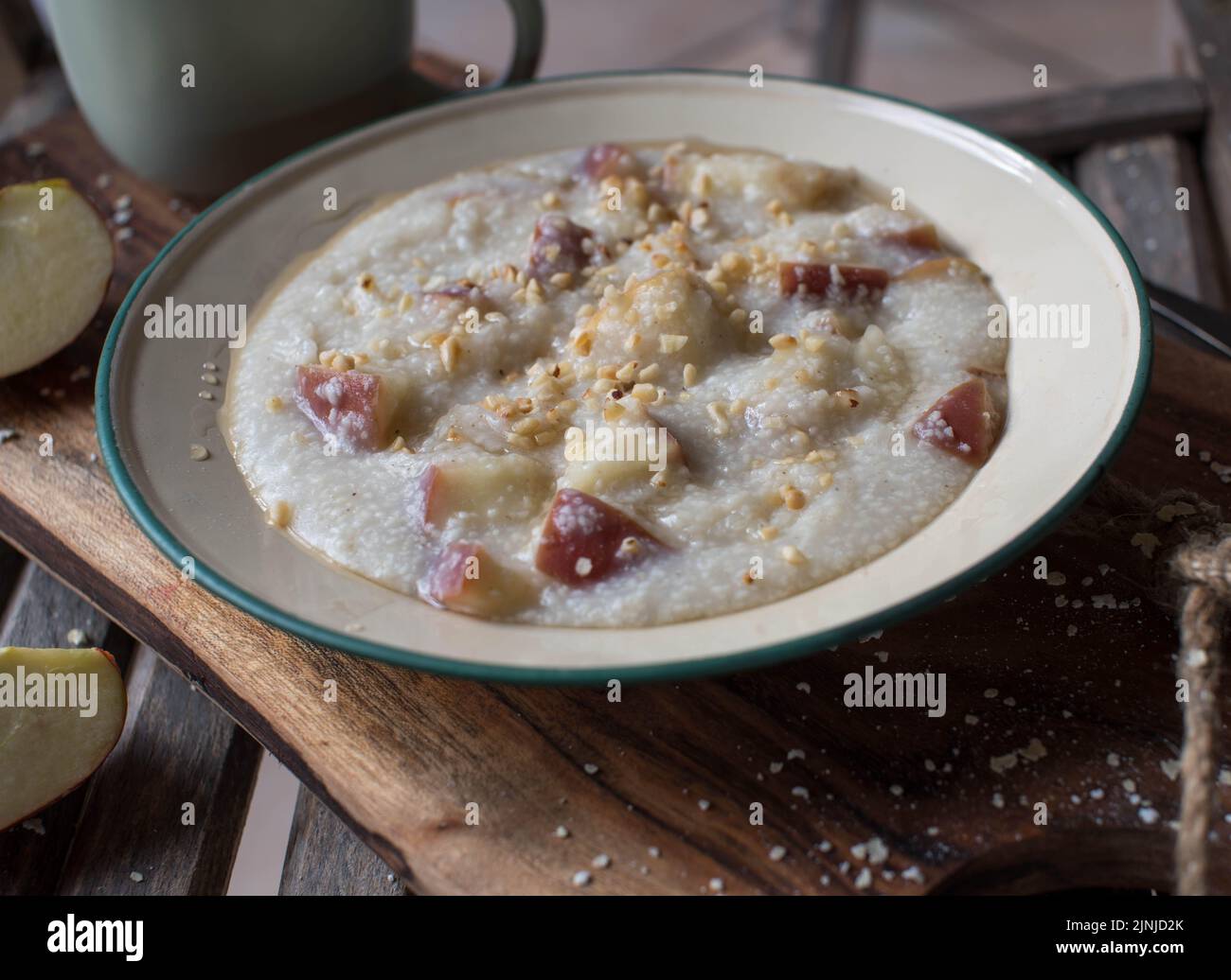 Petit déjeuner naturel avec porridge de millet frais, pommes, noisettes grillées et sirop d'érable. Servi sur une assiette ou un bol en émail à l'ancienne Banque D'Images