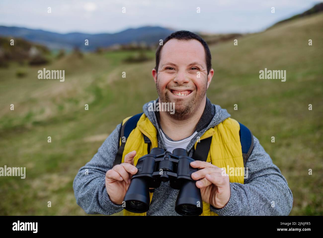 Portrait d'un jeune homme heureux avec le syndrome de Down en plein air, appréciant la nature et regardant à travers des jumelles. Banque D'Images
