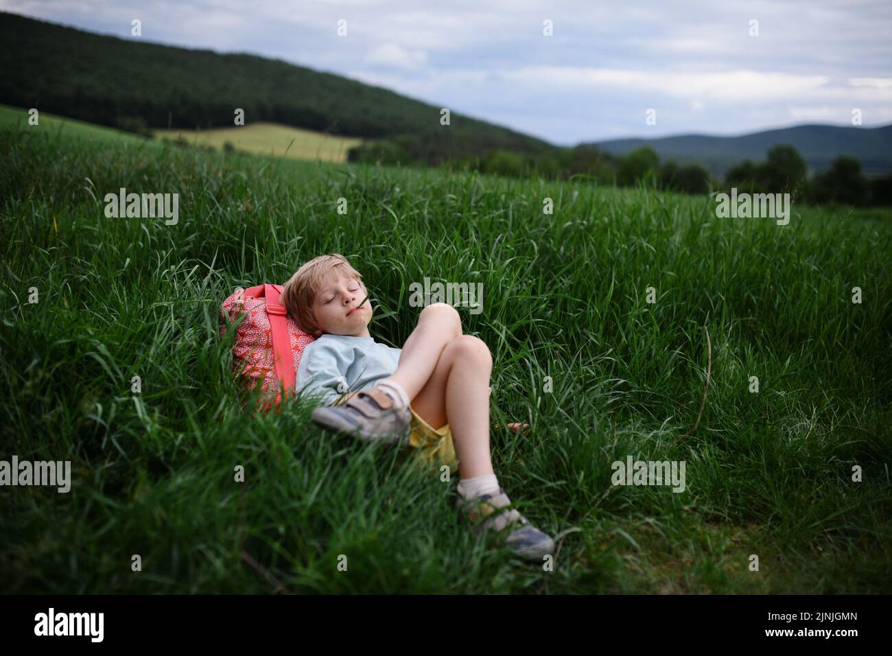 Bonne première journée d'école. Écolier fatigué avec sac à dos, repose sur l'herbe. Banque D'Images