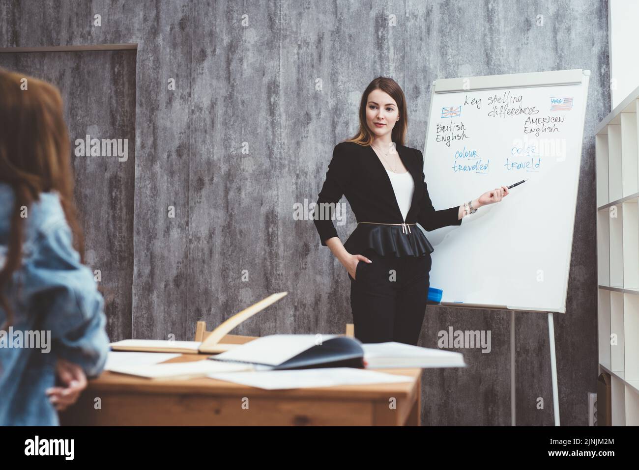 Professeur expliquant les différences entre l'orthographe américaine et britannique écrit sur tableau blanc tandis que des étudiants adultes assis au bureau l'écoutant en Banque D'Images