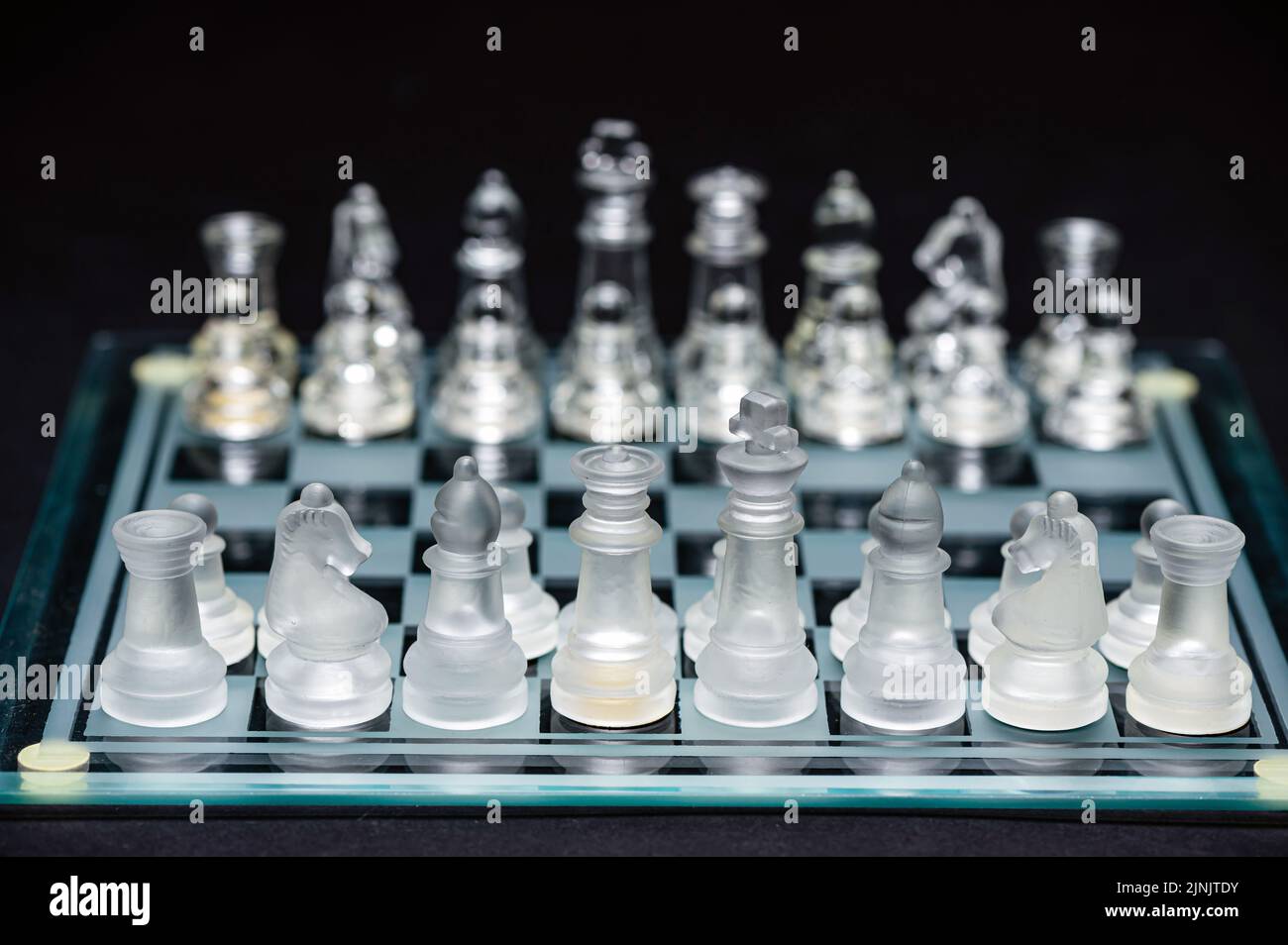 verre transparent, pièces d'échecs transparentes sur un damier, mise au point sélective, gros plan, isolé sur le noir Banque D'Images