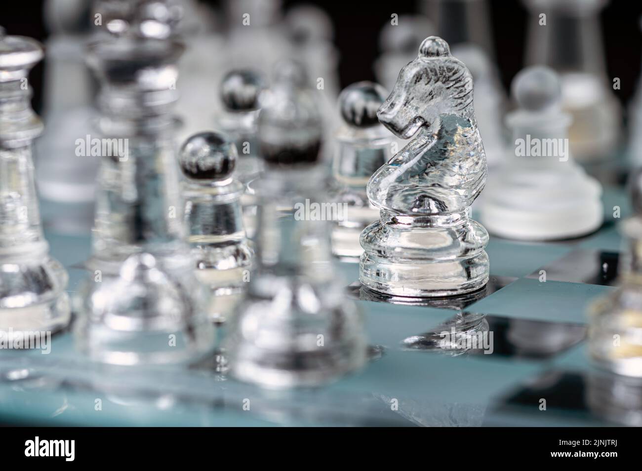 jeu d'échecs en verre transparent sur fond sombre, mise au point sélective sur la pièce de chevalier, gros plan Banque D'Images