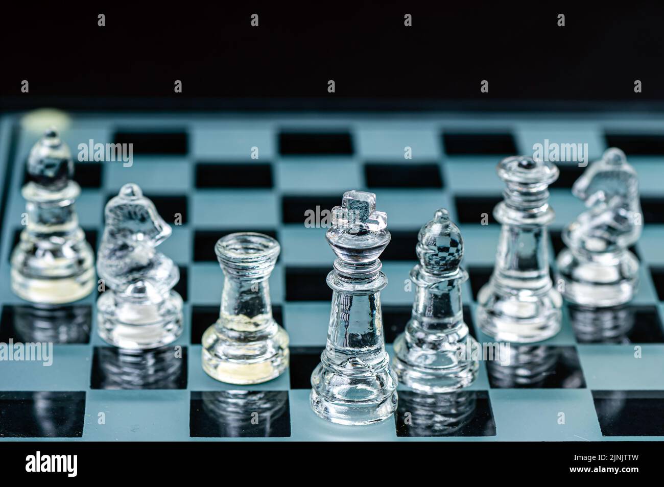 personnages d'échecs en verre transparent disposés en rangée et reflétant dans un échiquier en verre. Isolé sur le noir Banque D'Images