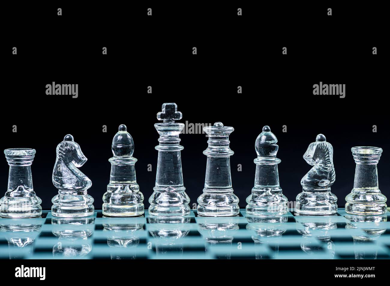 personnages d'échecs en verre transparent disposés en rangée et reflétant dans un échiquier en verre. Isolé sur le noir Banque D'Images