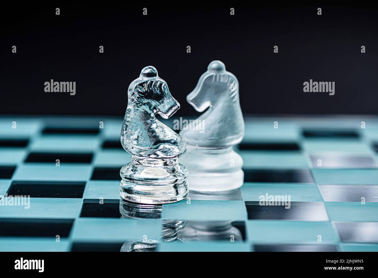 deux chevaliers d'échecs en verre opposés sur un plateau d'échecs en verre, fond noir, espace de copie Banque D'Images