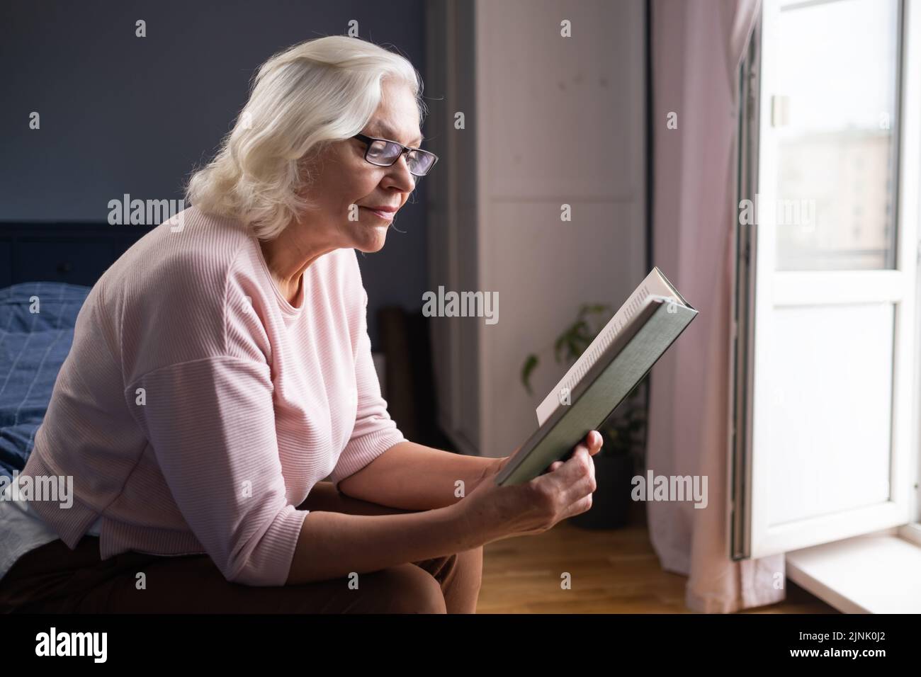 La vieille dame du caucase s'assoit sur le canapé pour lire un livre Banque D'Images