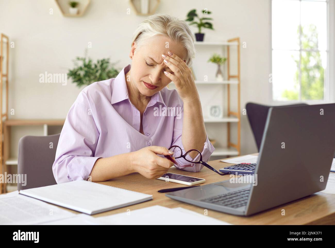 Une femme mature se sent fatiguée et souffre d'un mal de tête après avoir travaillé sur son ordinateur portable Banque D'Images
